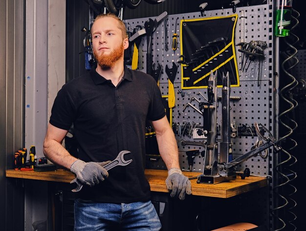 Portrait de mécanicien vélo barbu sur fond de support d'outil dans un atelier.