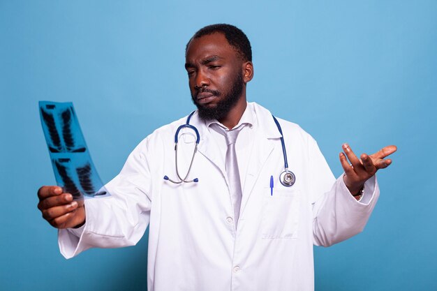 Portrait d'un médecin intrigué analysant un film radiographique thoracique pensant au diagnostic radiologique. Médecin ciblé en blouse blanche avec stéthoscope tenant une radiographie pulmonaire.