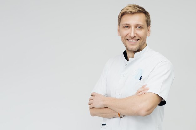 Portrait d'un médecin souriant les mains croisées devant un mur blanc