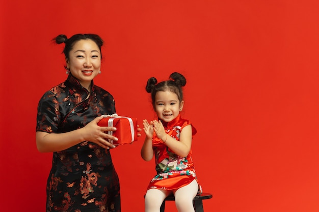 Portrait de mère et fille asiatique isolé sur un mur rouge en vêtements traditionnels