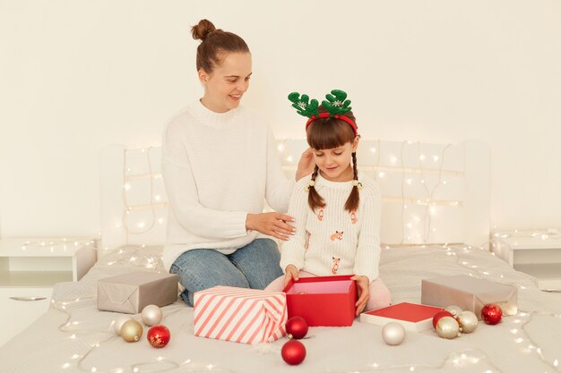 Portrait d'une mère heureuse et d'une petite fille ouvrant des cadeaux de Noël au lit à la maison, passant le réveillon du nouvel an ensemble, célébrant les vacances d'hiver, joyeux Noël.