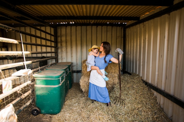 Photo gratuite portrait de mère portant sa fille debout près de la pile de foin