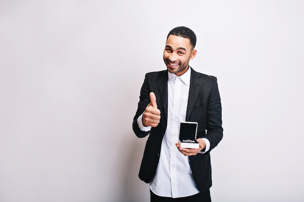 Portrait mignon beau mec en chemise blanche, veste noire avec cadeau en mains souriant. Exprimer de vraies émotions positives, une humeur joyeuse, un cadeau pour une petite amie, des bijoux.