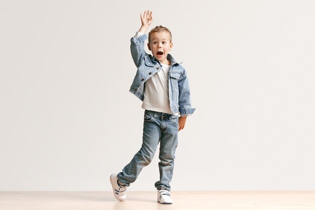 Le portrait de mignon petit garçon enfant dans des vêtements de jeans élégants regardant la caméra contre le mur blanc du studio. Concept de mode pour enfants