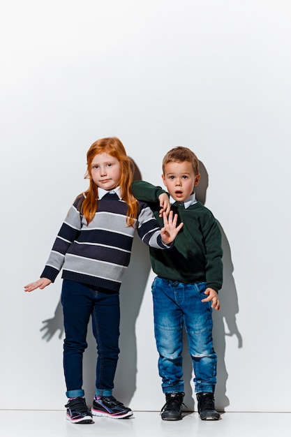 Le portrait de mignon petit garçon et fille en vêtements jeans élégants posant