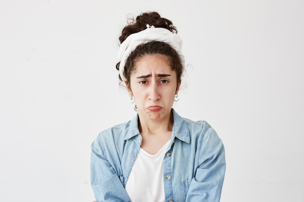 Portrait d'une misérable femme brune et sombre semble offensée, fronce les sourcils de mécontentement, entend des commentaires désagréables sur son travail. Jeune femme en chemise en jean abusée par des collègues ou des amis