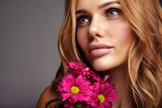 Portrait de mode de beauté du jeune mannequin femme blonde avec un maquillage naturel et une peau parfaite avec une fleur de chrysanthème сrimson brillant posant