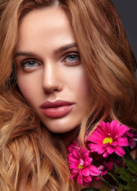 Portrait de mode de beauté du jeune mannequin femme blonde avec un maquillage naturel et une peau parfaite avec une fleur de chrysanthème сrimson brillant posant