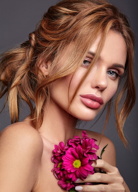 Portrait de mode de beauté du jeune mannequin femme blonde avec un maquillage naturel et une peau parfaite avec une fleur de chrysanthème сrimson brillant posant