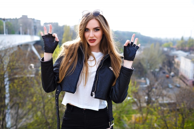 Portrait de mode grunge d'élégante femme blonde, veste de motard en cuir et gants, humeur rock n roll, vue urbaine sur le pont de la ville, mode de rue, maquillage de coiffure, voyageur.