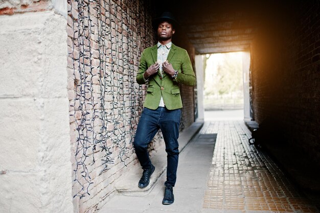 Portrait de mode d'un homme afro-américain noir sur une veste en velours vert chapeau noir posé au tunnel de la voûte au coucher du soleil