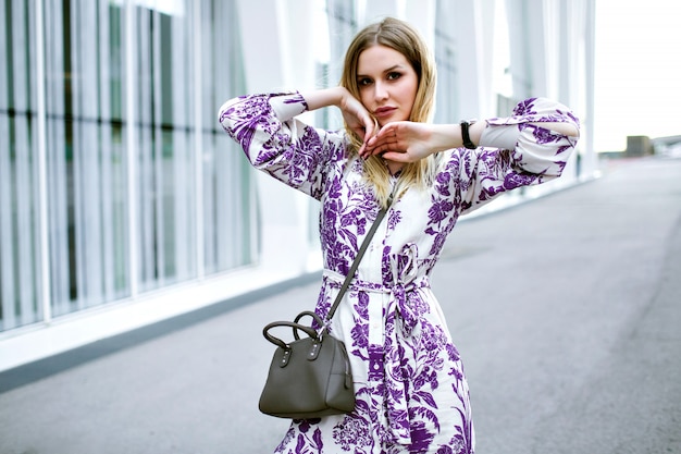 Photo gratuite portrait de mode de mode de vie d'élégante jolie femme blonde posant dans la rue près du centre d'affaires moderne, portant un sac et des accessoires de robe florale glamour, des couleurs douces.