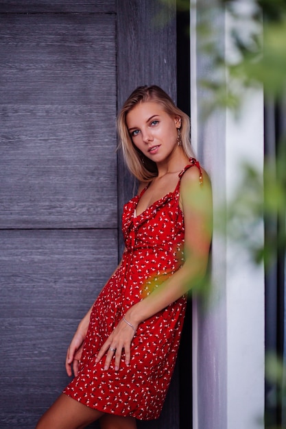 Portrait de mode en plein air beauté naturelle jeune jolie femme avec léger maquillage, boucles d'oreilles étoiles, bracelet et bague. Femme en robe de fleurs d'été rouge