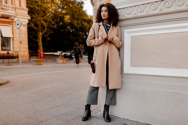 Portrait de mode en plein air de glamour sensuelle jeune femme noire élégante portant une tenue d'automne à la mode, un pull en velours gris et un manteau en laine beige.