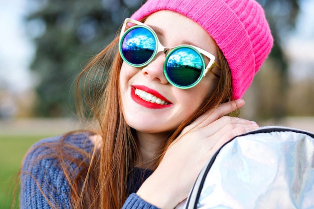 Portrait de mode positif en plein air de superbe belle femme au gingembre, posant au parc de la ville, portant un chapeau hipster et la météo, des lunettes de soleil de luxe à la mode, des jeunes, des vacances, des lèvres rouges, des couleurs pastel.