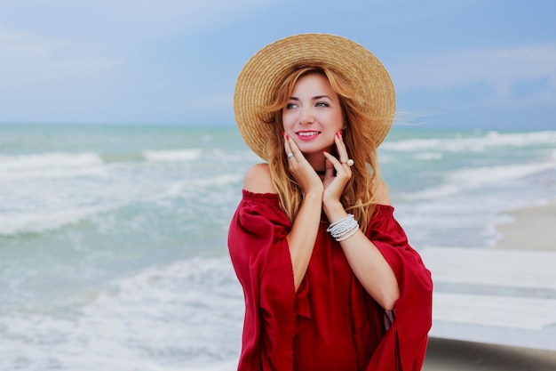 Portrait de mode de vie en plein air de jolie femme au gingembre blanc en robe élégante posant sur la plage près de l'océan. Ciel bleu. Temps venteux.