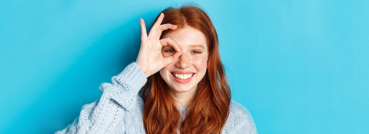 Photo gratuit portrait d'un modèle féminin rousse joyeux montrant un signe correct sur l'oeil souriant satisfait et heureux sta