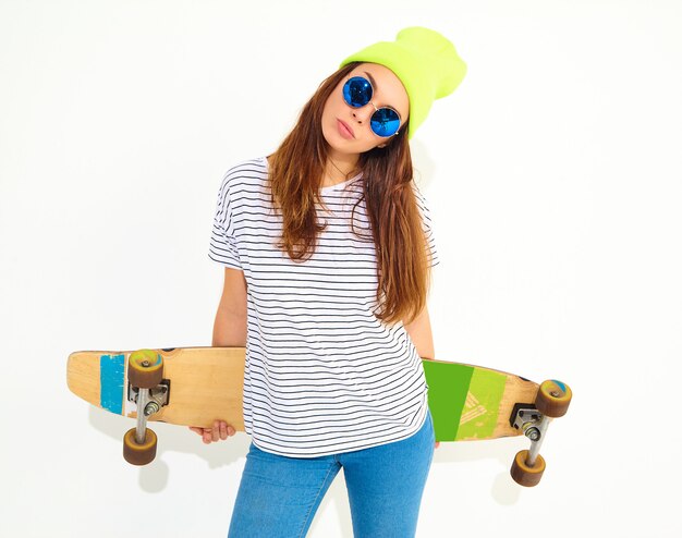 Portrait de modèle jeune femme élégante dans des vêtements d'été décontractés en bonnet jaune posant avec bureau longboard. Isolé sur blanc