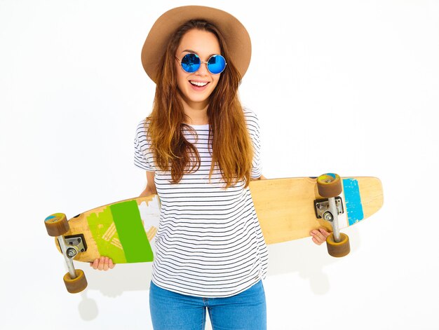 Portrait de modèle jeune femme élégante dans des vêtements d'été décontractés en chapeau brun posant avec bureau longboard. Isolé sur blanc