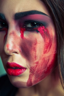Portrait d'un monstre monstre avec un maquillage de couleur sale sur son visage. femme qui pleure avec des larmes sanglantes rouges et la main. concept d'halloween sur fond vert. tourné en studio, yeux marron foncé.