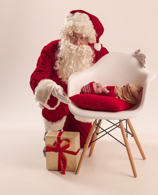 Portrait de Noël de mignonne petite fille nouveau-né, vêtue de vêtements de Noël et homme portant un costume et un chapeau de père Noël, tourné en studio, heure d'hiver. Le concept de Noël, vacances
