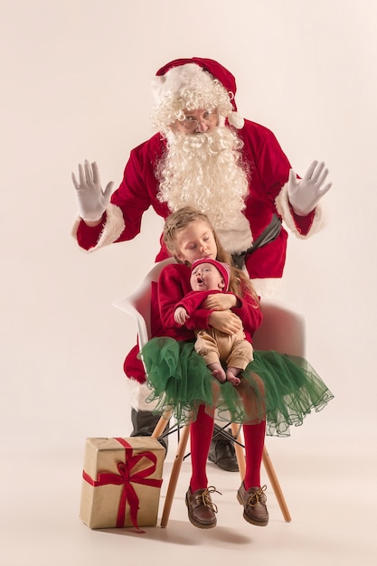 Portrait de Noël de mignonne petite fille nouveau-née, jolie soeur adolescente, vêtue de vêtements de Noël et homme portant un costume et un chapeau de père Noël, tourné en studio, heure d'hiver. Le concept de Noël, vacances