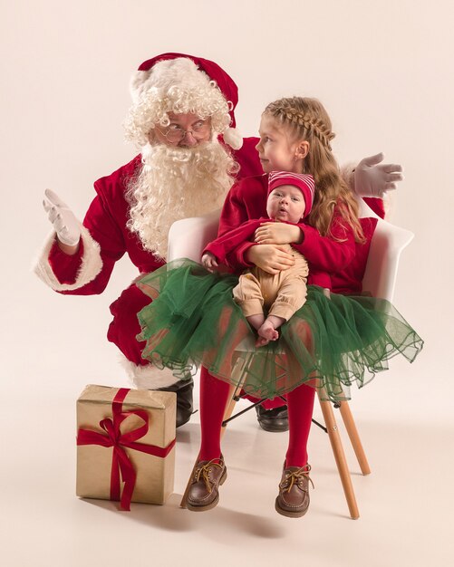 Portrait de Noël de mignonne petite fille nouveau-née, jolie soeur adolescente, vêtue de vêtements de Noël et homme portant un costume et un chapeau de père Noël, tourné en studio, heure d'hiver. Le concept de Noël, vacances