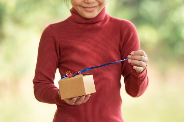 Portrait de Noël d'une petite fille souriante et heureuse avec une boîte-cadeau près d'une branche verte. feuilles vertes bokeh flou fond de forêt nature.