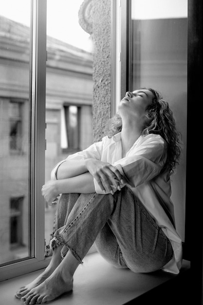 Portrait noir et blanc d'une belle femme posant à l'intérieur sur un rebord de fenêtre