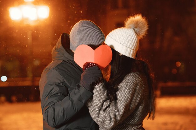 Portrait de nuit en plein air de jeune couple avec coeur de papier dans la rue