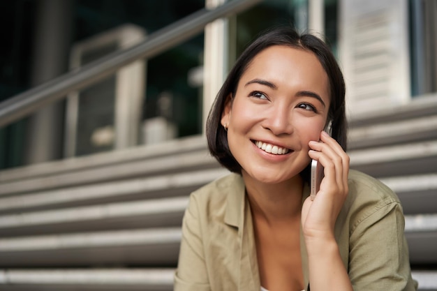 Photo gratuite portrait of asian girl sourit tout en pourparlers sur téléphone mobile jeune femme appelant un ami assis sur st