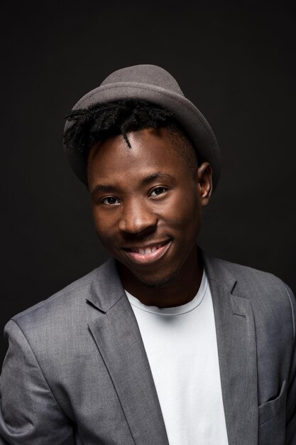 Portrait of attractive young black male studio with hat sourire ringard sur fond sombre