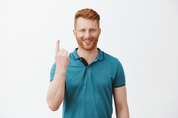 Portrait of confiant beau homme rousse masculin européen mature avec poils en polo vert, montrant le numéro un avec l'index et souriant heureux