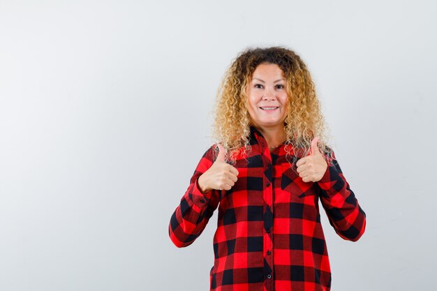 Portrait of cute blonde woman showing double Thumbs up en chemise à carreaux et à la vue de face heureux