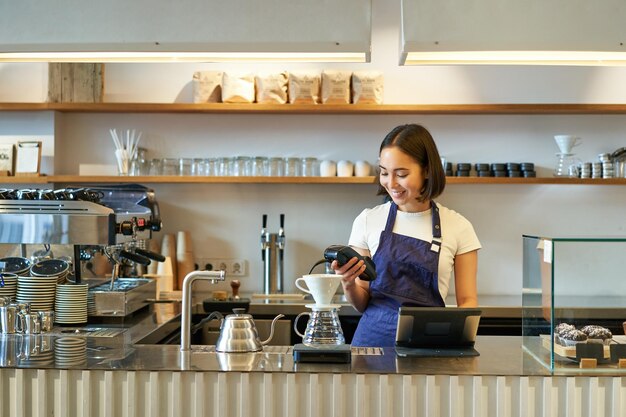 Portrait of cute girl student travaille comme barista détient une machine à carte de crédit pos debout au comptoir wit