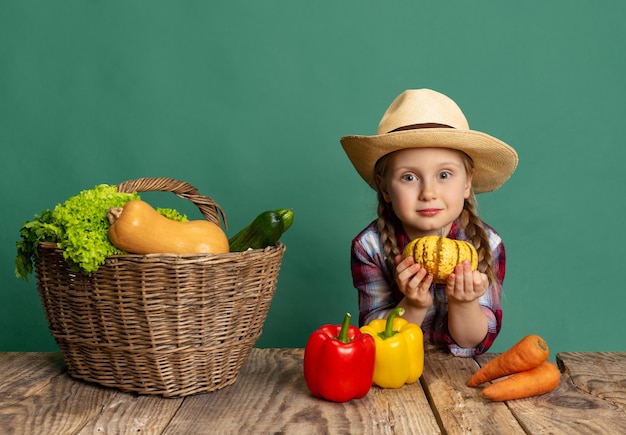 Portrait of cute little girl in image of farmer posant avec des légumes isolés sur fond vert