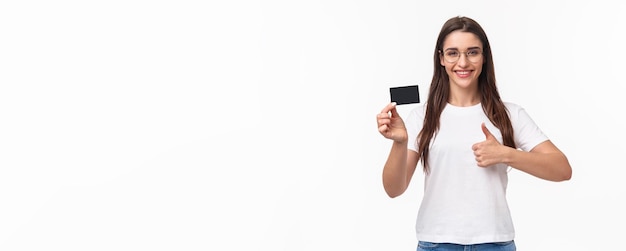 Portrait of happy attractive young brunette woman in tshirt et lunettes recommande banque montrant cre