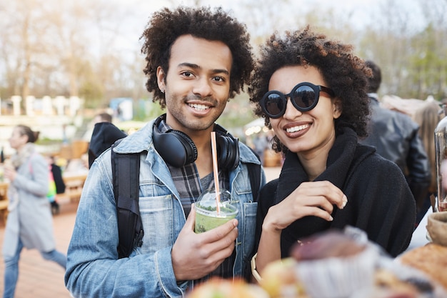 Portrait of happy cute couple à la peau foncée avec une coiffure afro, se promener sur le festival de la nourriture, dégustation et boire un cocktail