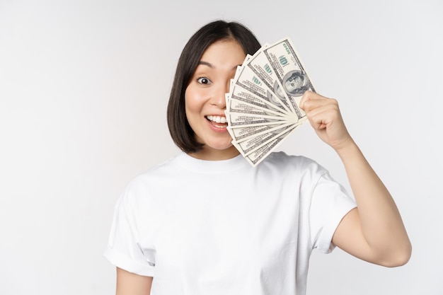 Portrait of smiling asian woman holding dollars argent concept de financement de microcrédit et de trésorerie debout sur fond blanc