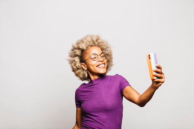 Portrait of smiling young woman using smart phone avec un cas de drapeau arc-en-ciel en se tenant debout contre wh
