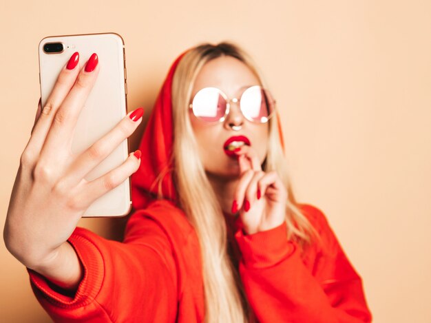 Portrait of young beautiful hipster bad girl in trendy jeans clothing and earring in her nose. Sexy insouciant smiling blonde woman takes selfie.