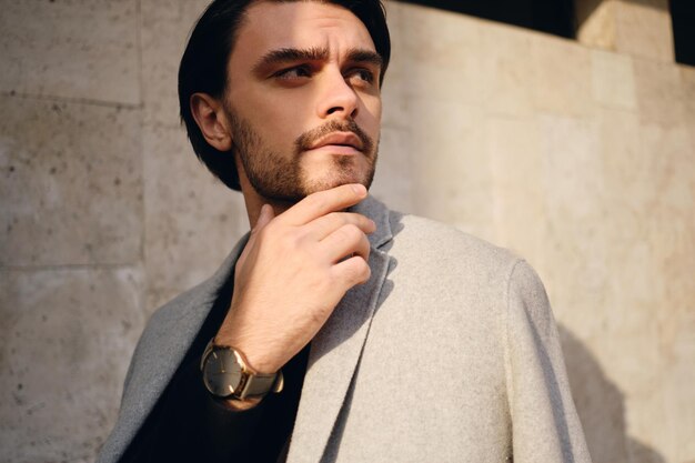 Portrait of young brunette man in coat pensivement à l'écart en plein air