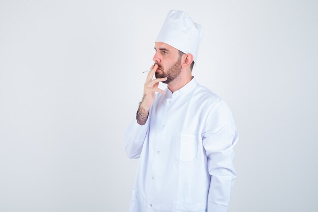 Portrait of young male chef smoking cigarette en uniforme blanc et à la vue de face réfléchie