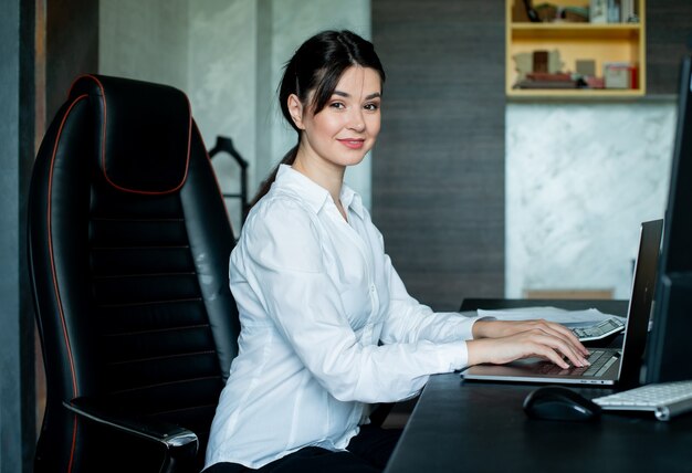 Portrait of young office worker woman sitting at office desk using laptop computer looking at camera smiling joyeusement travaillant au bureau