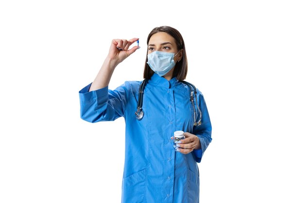 Portrait of young woman medical worker looking at pill isolated over white background studio