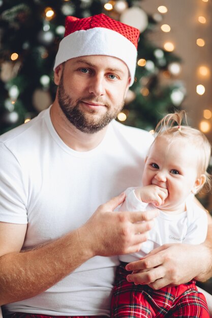 Portrait d'un papa barbu aimant en bonnet rouge tenant une petite fille mignonne dans les bras.