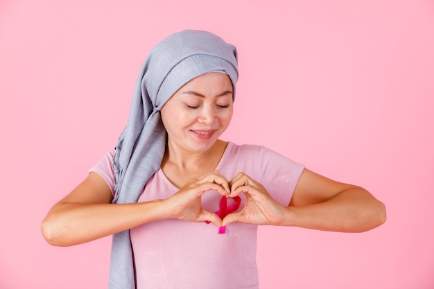 Portrait d'une patiente asiatique atteinte d'un cancer du sein en montrant des mains en forme de coeur geste ruban rose isolé sur fond de studio espace copie vierge rose, soins de santé, concept de médecine