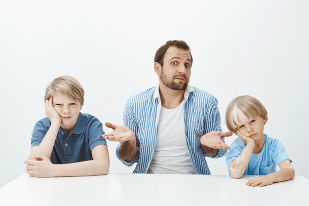 Portrait de père européen inconscient confus assis avec des fils à table