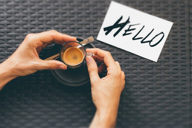 Portrait d'une personne buvant une tasse de café près d'une impression bonjour sur une carte blanche