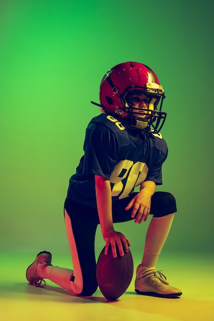 Portrait d'un petit garçon enfant jouant au football américain de formation isolé sur fond vert en néon